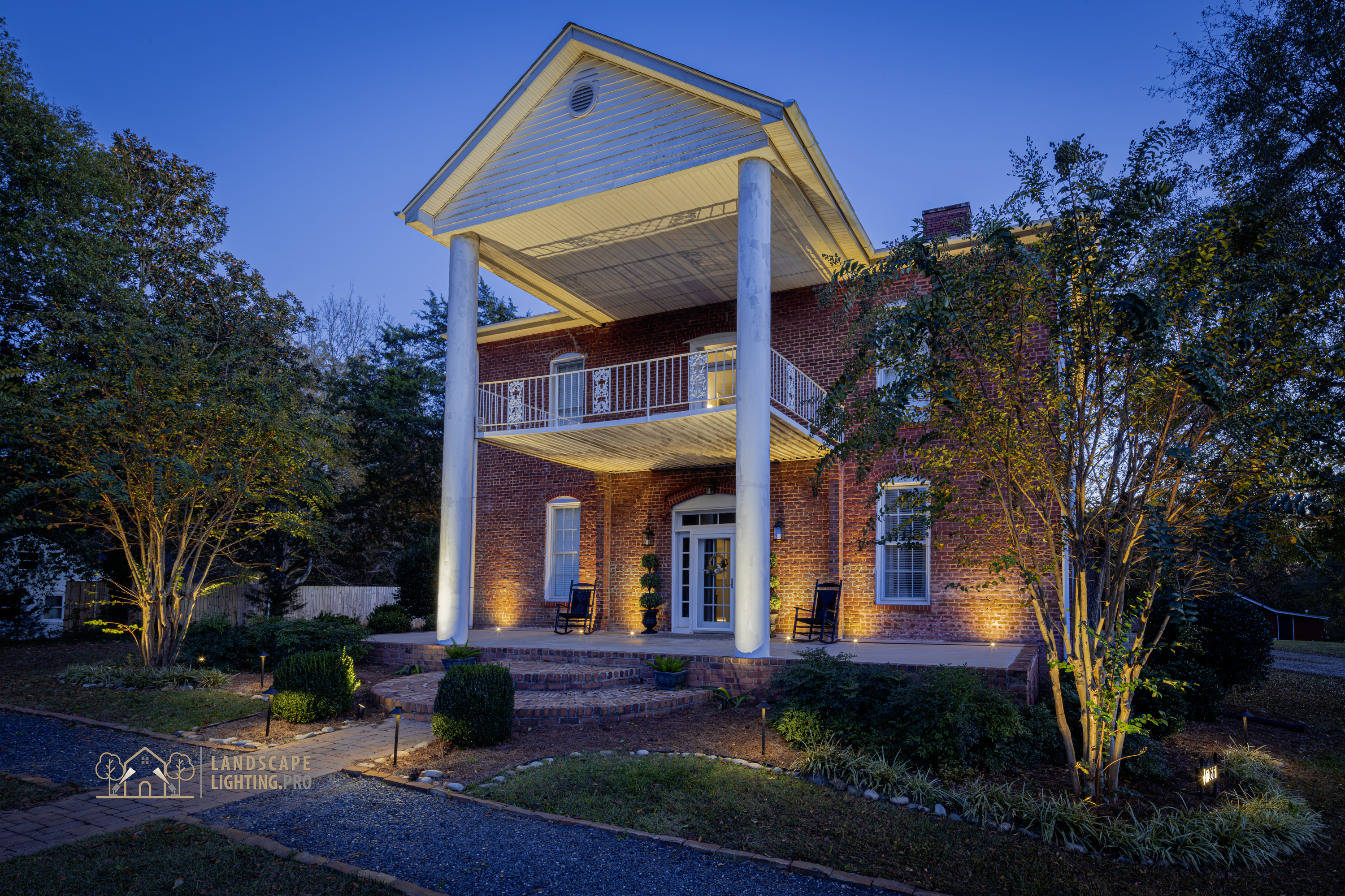 An 1850 historic brick home illuminated at dusk with embedded landscape lighting